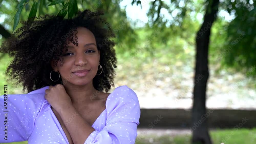 a young African woman in a lilac top with ties and puffy sleeves dances under green trees. close up a young African woman in a lilac top with ties and puffy sleeves dances under green trees. close up