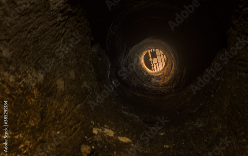 Image of the body of a well portrayed from the bottom. View of the grating at the top  on the mouth.
