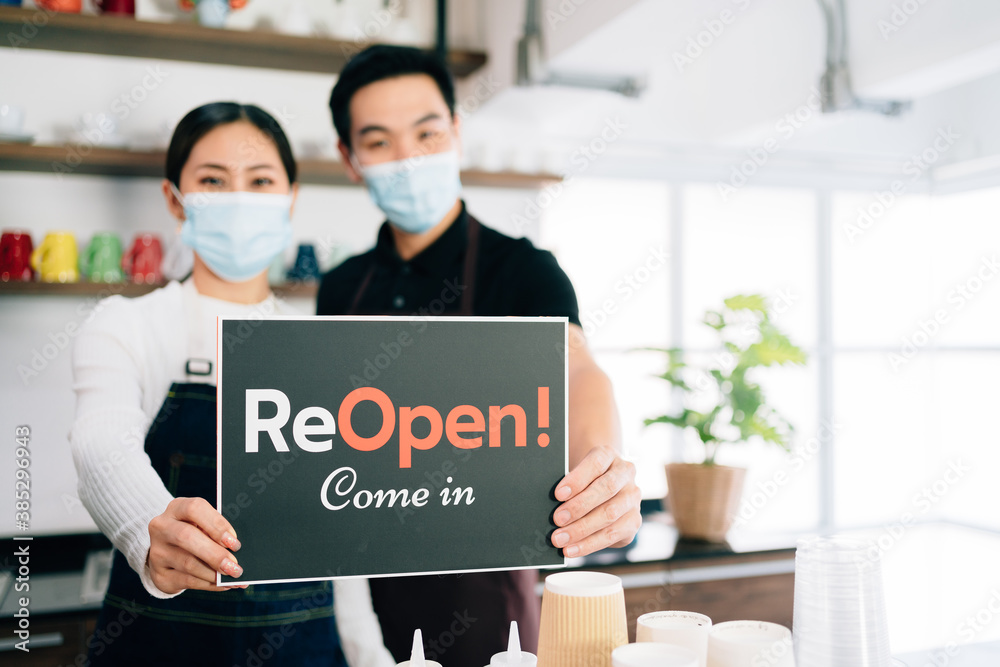 Young baristas couple wearing mask opening their own cafe, making announcements with a sign on a board Young baristas couple wearing mask opening their own cafe, making announcements with a sign on a board