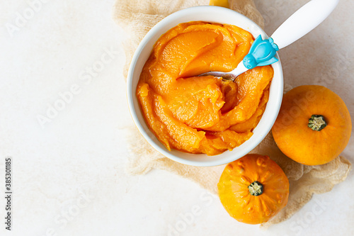 Fotomural Homemade pumpkin puree in bowl with baby spoon and fresh pumpkins on light concrete background
