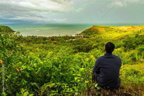 man sitting at hilltop with landscape serene view and dense green forests