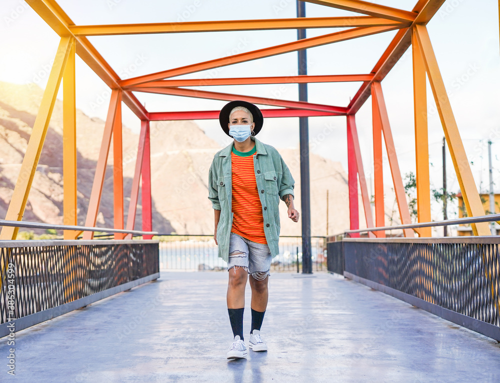 Happy latin hipster girl walking outdoor while wearing surgical face mask - Coronavirus lifestyle
