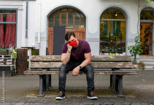 Junger Mann mit Rote Gesichtsmaske auf einer Bank sitzend photo