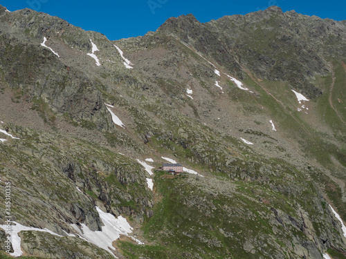 view on Nurnberger Hutte mountain hut at steep slope of snow-capped peaks at Stubai hiking trail, Stubai Hohenweg, Summer rocky alpine landscape of Tyrol, Stubai Alps, Austria photo