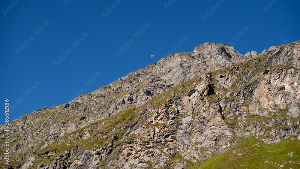 Mond am blauen Himmel über einer Felswand in den Hohen Tauern, Österreich Mond am blauen Himmel über einer Felswand in den Hohen Tauern, Österreich