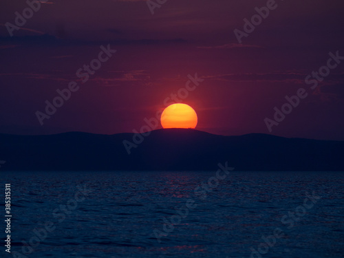 Sun setting behind a mountain by the coast