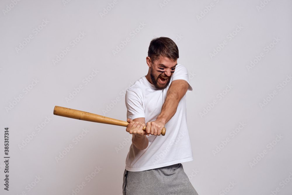 An emotional man with a baseball bat on a light background in a white T-shirt is gesturing with his hands to the model An emotional man with a baseball bat on a light background in a white T-shirt is gesturing with his hands to the model