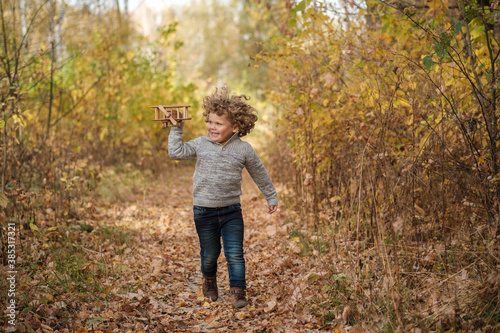 cute curly haired boy playing with wooden plane in autumn park