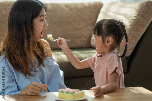 Asian younger sister feeding her older sister with spoon of tasty cake