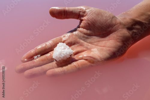 Hand holding white salt crystal in pink vibrant salty water sunny close-up. Spa procedures in natural resort on Syvash, Ukraine © Kathrine Andi