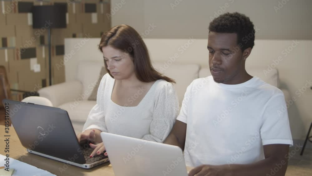 Couple of professionals sitting together at table, working in silence, typing on laptops. Medium shot. Co-working concept Couple of professionals sitting together at table, working in silence, typing on laptops. Medium shot. Co-working concept