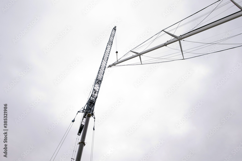 Superyacht. Sailing yacht. Placing of the mast. Cranes. Shipbuilding industry. Mast hanging in crane. Superyacht. Sailing yacht. Placing of the mast. Cranes. Shipbuilding industry. Mast hanging in crane.