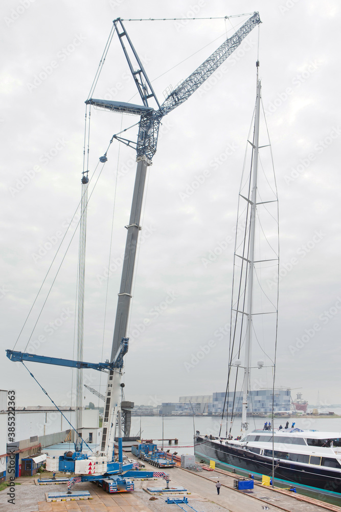 Superyacht. Sailing yacht. Placing of the mast. Cranes. Shipbuilding industry. Mast hanging in crane. Superyacht. Sailing yacht. Placing of the mast. Cranes. Shipbuilding industry. Mast hanging in crane.