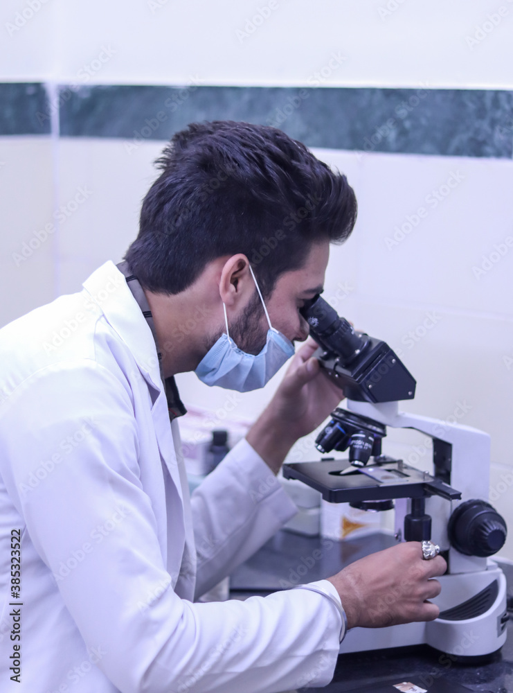 Devpura, Tonk, Rajasthan- October 14, 2020: Selective focus on Portrait of young indian doctor looking in microscope while working on medical research in science laboratory.