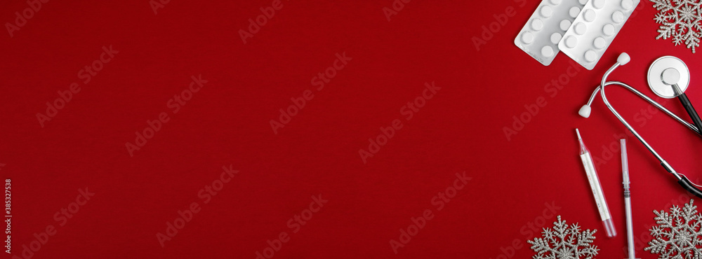 Medical Christmas background. Stethoscope, pills, blister, thermometer and syringe, on a red background with snowflakes. Banner. Flatly. Copy space