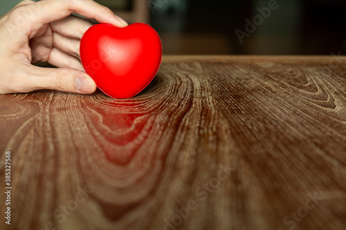 Hand holding a red heart on wooden table. Red heart in man hands. Woman hand red heart on wooden table. Love  health care  family  insurance  donation concept.