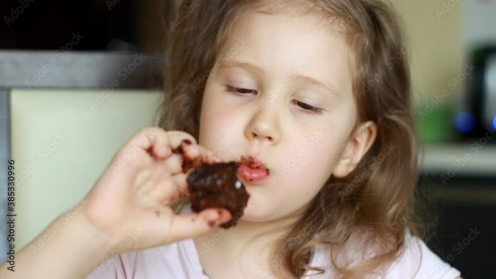Cute baby girl eating brownie. Child eats with appetite chocolate dessert. Closeup portrait. Cute baby girl eating brownie. Child eats with appetite chocolate dessert. Closeup portrait.