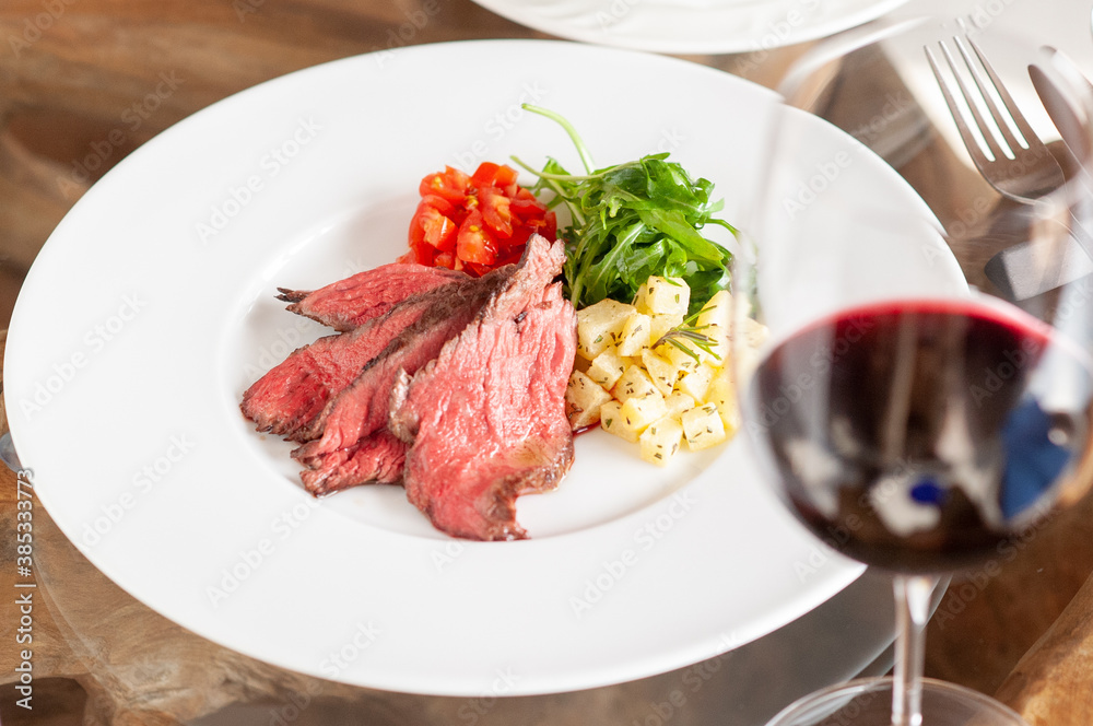 プレートに乗った肉料理と、付け合わせの野菜と赤ワイン プレートに乗った肉料理と、付け合わせの野菜と赤ワイン