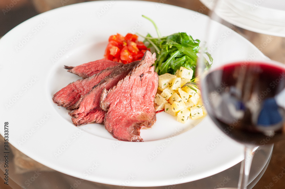 プレートに乗った肉料理と、付け合わせの野菜と赤ワイン プレートに乗った肉料理と、付け合わせの野菜と赤ワイン