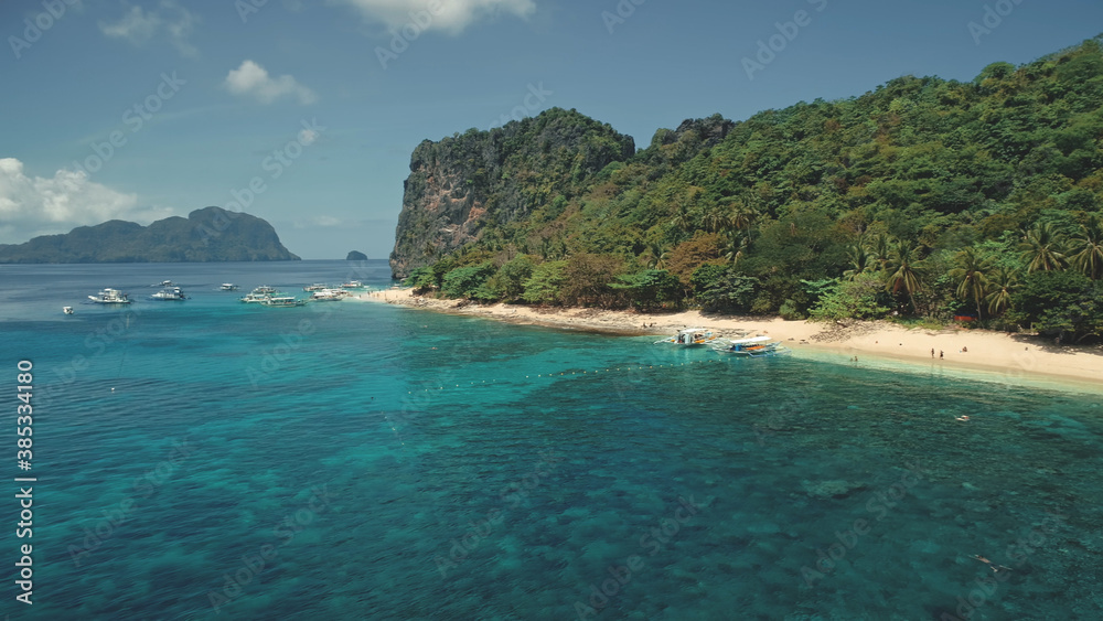 Fototapeta premium Ocean bay harbour with boats and passengers at sand beach aerial view. Panoramic landscape of tropic island with tourist. Green forest at shore with travelers at vessels on Palawan Isle, Philippines