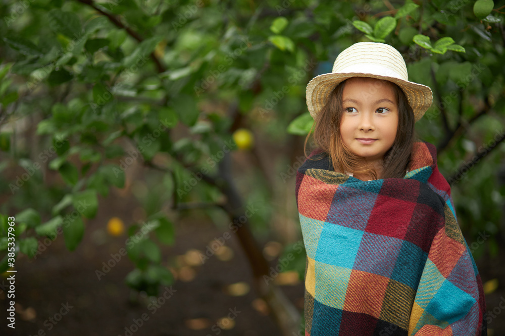 cute kid girl warming herself with a blanket in the forest, in nature. asian little girl posing at camera, surrounded by green plants and trees