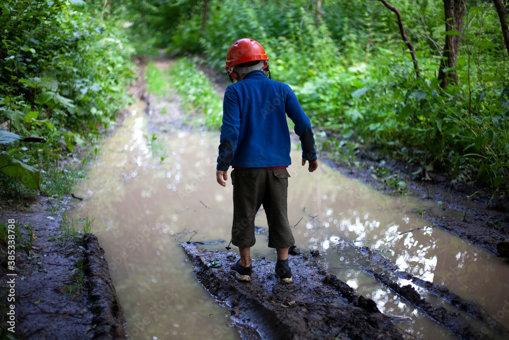 Child's Boy stands by a large puddle in the park. A child in a construction helmet. Lost son. 