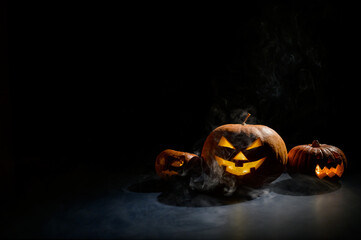 Halloween card. jack o lantern with candles glow on a black background. A row of creepy pumpkins with carved grimaces smokes in the dark.