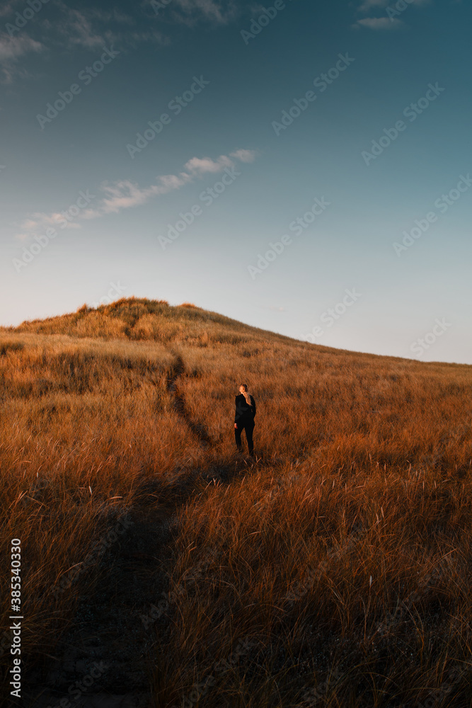 A active outdoor girl exploring a path in the orange grass sand dunes with colorful and beautiful sunset light. National Park Thy in Denmark, North Sea