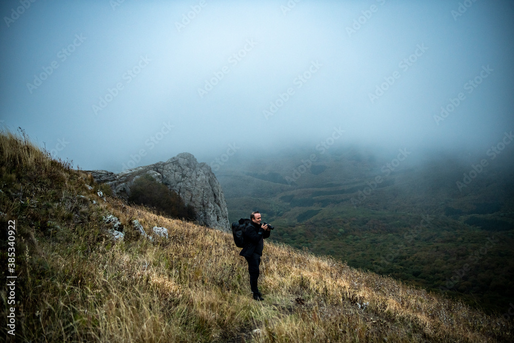 a tourist with a camera on a mountainside against the backdrop of fog and sunset