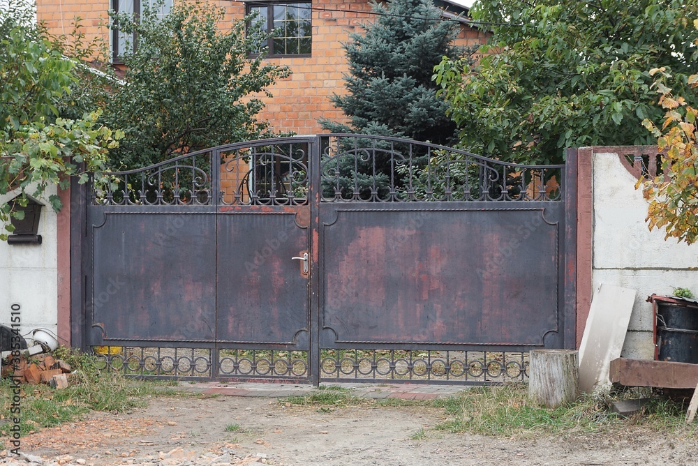 one closed brown iron gate and part of a white concrete fence on a rural street one closed brown iron gate and part of a white concrete fence on a rural street