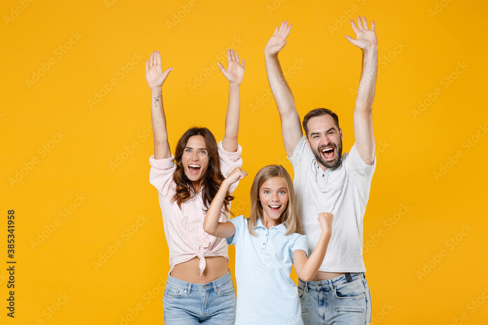 Joyful parents mom dad with child kid daughter teen girl in basic t-shirts rising hands doing winner gesture isolated on yellow background studio portrait. Family day parenthood childhood concept. Joyful parents mom dad with child kid daughter teen girl in basic t-shirts rising hands doing winner gesture isolated on yellow background studio portrait. Family day parenthood childhood concept.