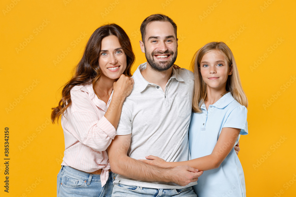 Smiling young happy parents mom dad with child kid daughter teen girl in basic t-shirts hugging looking camera isolated on yellow background studio portrait. Family day parenthood childhood concept. Smiling young happy parents mom dad with child kid daughter teen girl in basic t-shirts hugging looking camera isolated on yellow background studio portrait. Family day parenthood childhood concept.