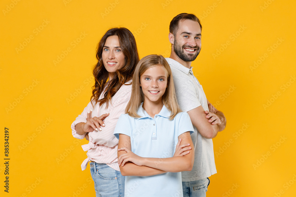 Smiling young happy parents mom dad with child kid daughter teen girl in basic t-shirts holding hands crossed isolated on yellow background studio portrait. Family day parenthood childhood concept. Smiling young happy parents mom dad with child kid daughter teen girl in basic t-shirts holding hands crossed isolated on yellow background studio portrait. Family day parenthood childhood concept.