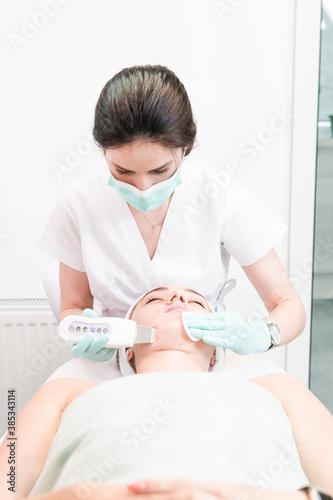 The female cosmetologist makes a procedure of ultrasonic cleaning face, close-up. Young woman in a beauty salon. Concept of cosmetology and professional skin care