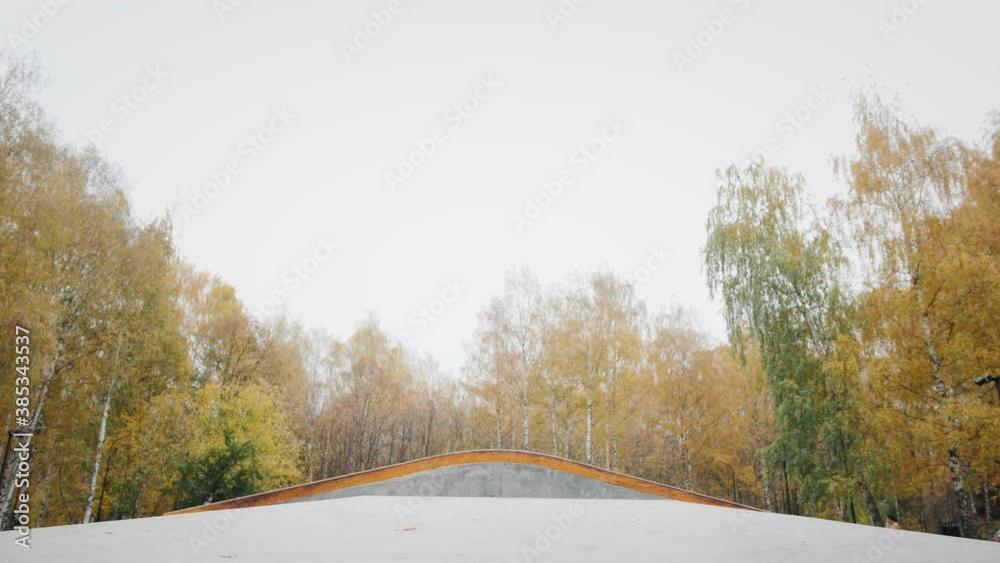 Skater practicing in the autumn concrete skate park, making tricks and rides in ramp. Skateboarder making tricks, manual balance, boardslide and stalls, professional extreme sport Skater practicing in the autumn concrete skate park, making tricks and rides in ramp. Skateboarder making tricks, manual balance, boardslide and stalls, professional extreme sport