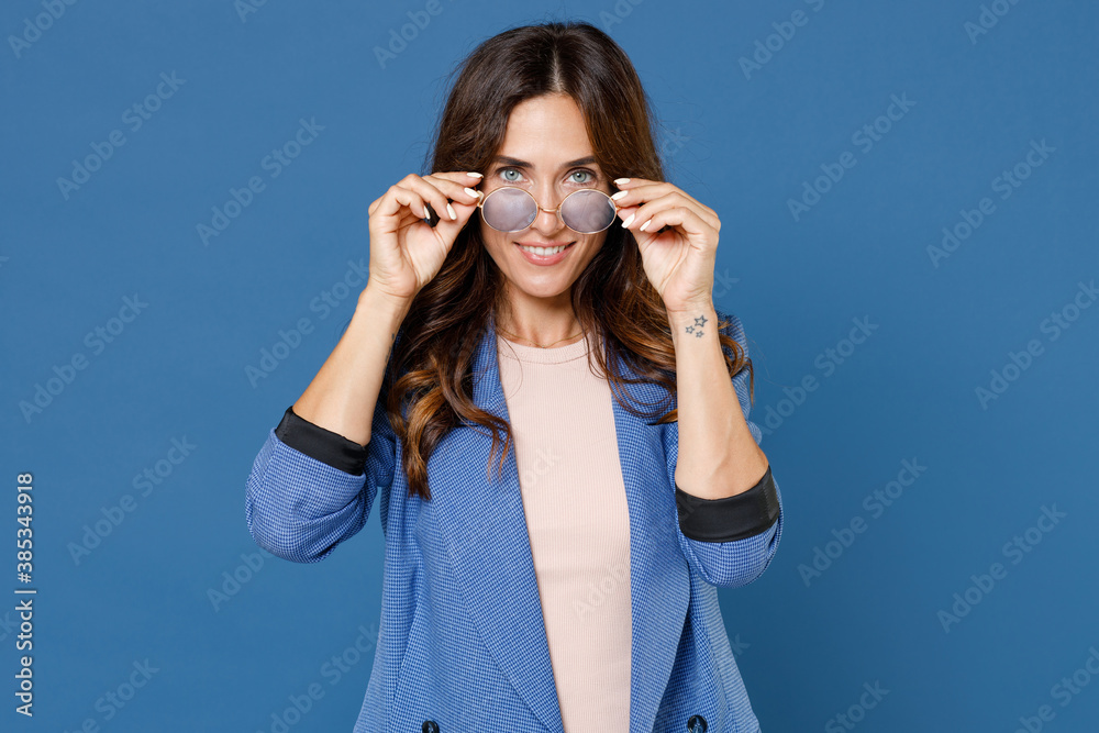 Smiling successful confident beautiful attractive young brunette woman 20s wearing basic jacket eyeglasses standing and looking camera isolated on bright blue colour wall background, studio portrait. Smiling successful confident beautiful attractive young brunette woman 20s wearing basic jacket eyeglasses standing and looking camera isolated on bright blue colour wall background, studio portrait.