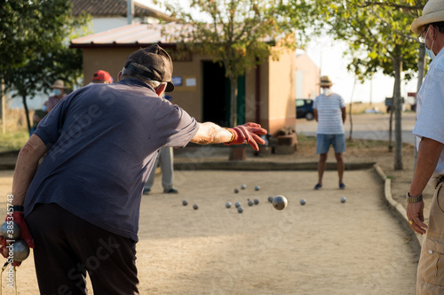 Old man wearing gloves playing petanque outdoors. photo
