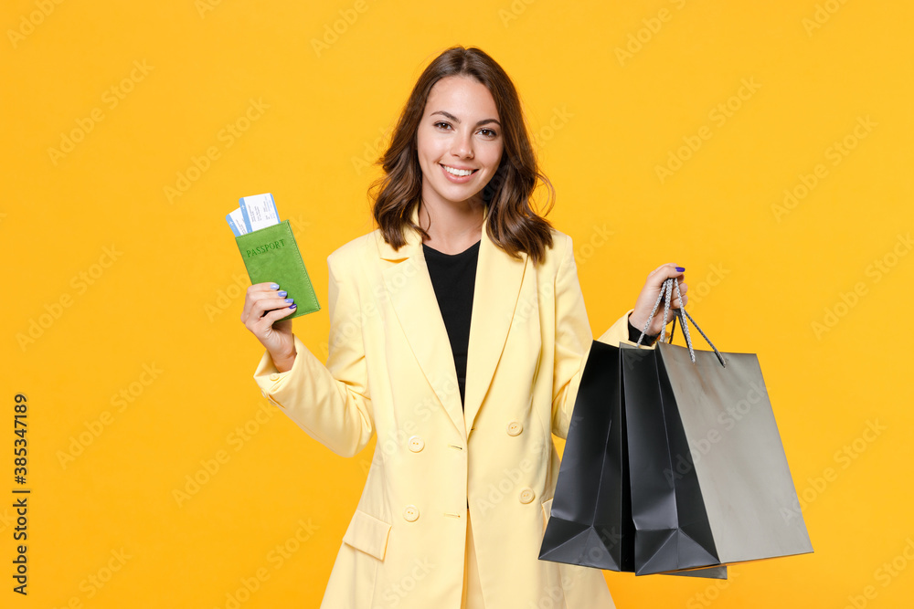 Smiling young woman wearing basic light suit jacket hold package bags with purchases after shopping passport tickets boarding pass isolated on yellow background, studio portrait. Black friday sale. Smiling young woman wearing basic light suit jacket hold package bags with purchases after shopping passport tickets boarding pass isolated on yellow background, studio portrait. Black friday sale.