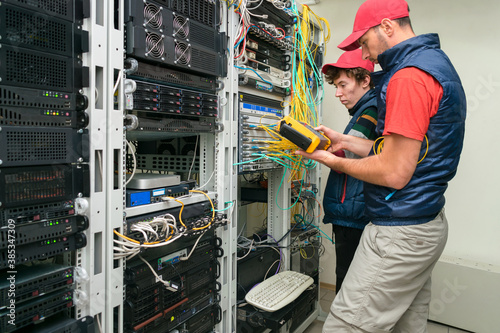 Two technicians measure the signal level in the fiber optic cable. Serving a central router in a server room. Two people work in a modern data center.