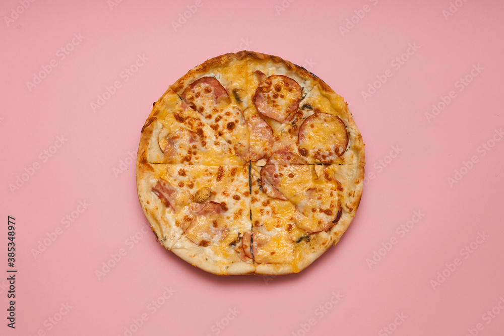 Fototapeta Round, cut into pieces, Italian pizza with cheese and salami. Shooting from above. Pink background.
