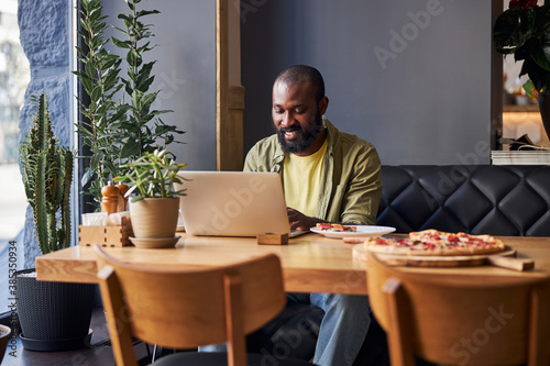 Joyful Afro American man using modern laptop in cafe