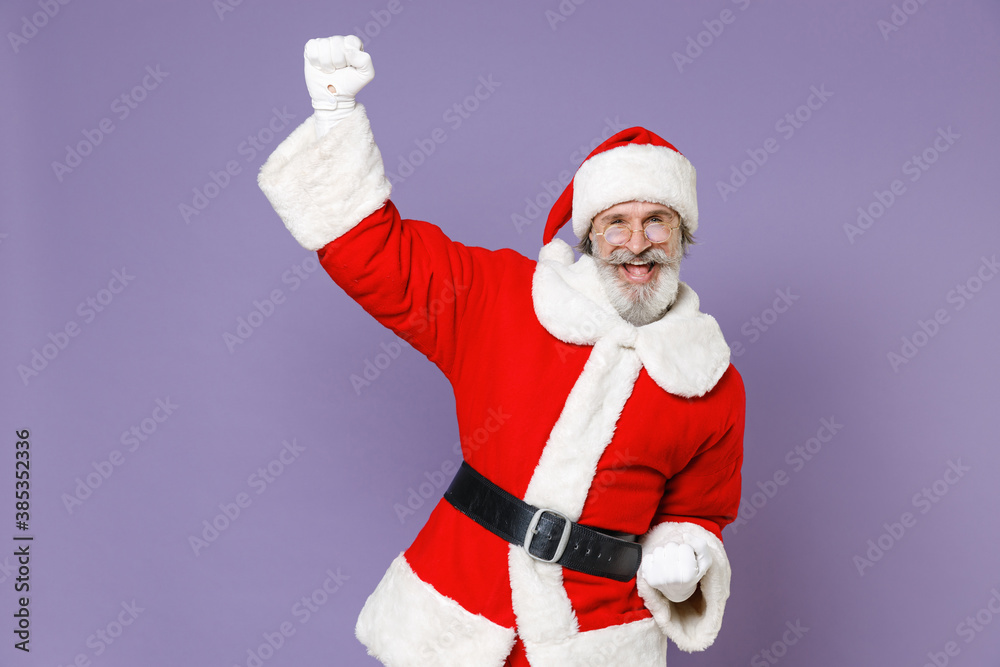 Overjoyed Santa Claus man in Christmas hat red coat white gloves glasses  clenching fists doing winner gesture isolated on violet background studio.  Happy New Year celebration merry holiday concept. Stock Photo