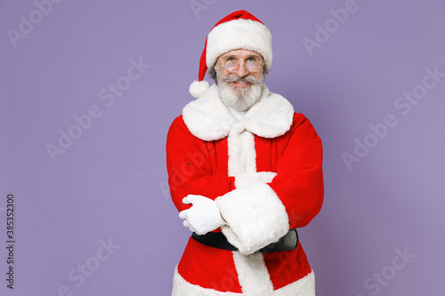 Smiling gray-haired Santa Claus man in Christmas hat red suit coat white gloves glasses holding hands crossed isolated on violet background studio. Happy New Year celebration merry holiday concept.