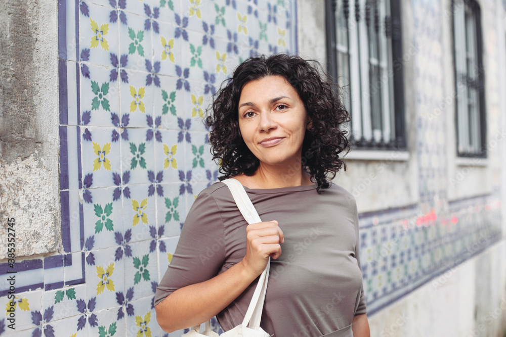 A woman with curly hair walking in a town of Portugal. A wall with traditional Portuguese tiles - azulejo