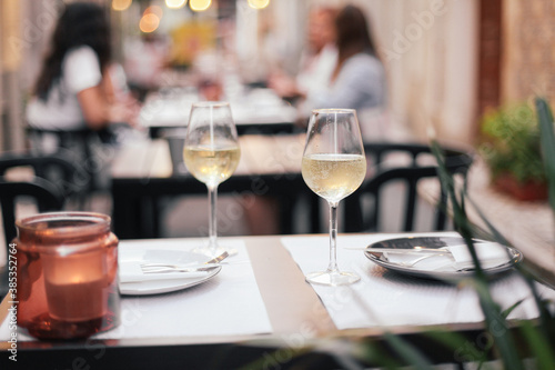 Two glasses on white wine and a candle on a restaurant outdoor table, evening lights on a cozy European street