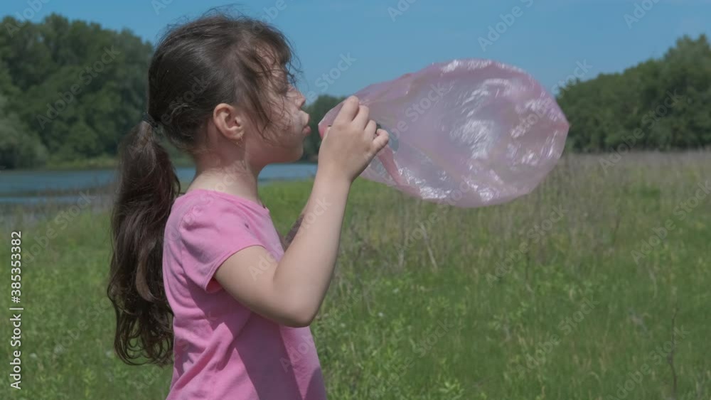 A child with a plastic bag. Little girl blows into a plastic bag outdoors. Stock ビデオ | Adobe Stock