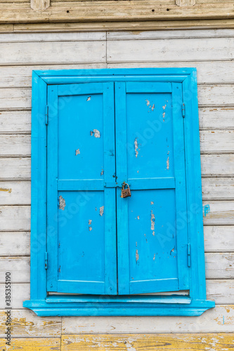 locked blue window on an old wooden house © dadamira