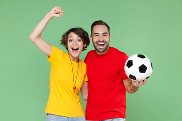 Laughing funny young couple friends sport family woman man football fans in t-shirts cheer up support favorite team with soccer ball expressive gesticulating hands isolated on green background studio.