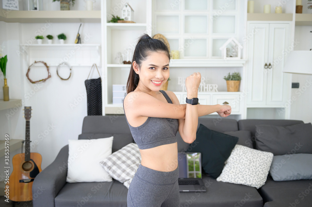 A happy young woman in sportswear is doing stretching and warming up on mat in living room at home A happy young woman in sportswear is doing stretching and warming up on mat in living room at home