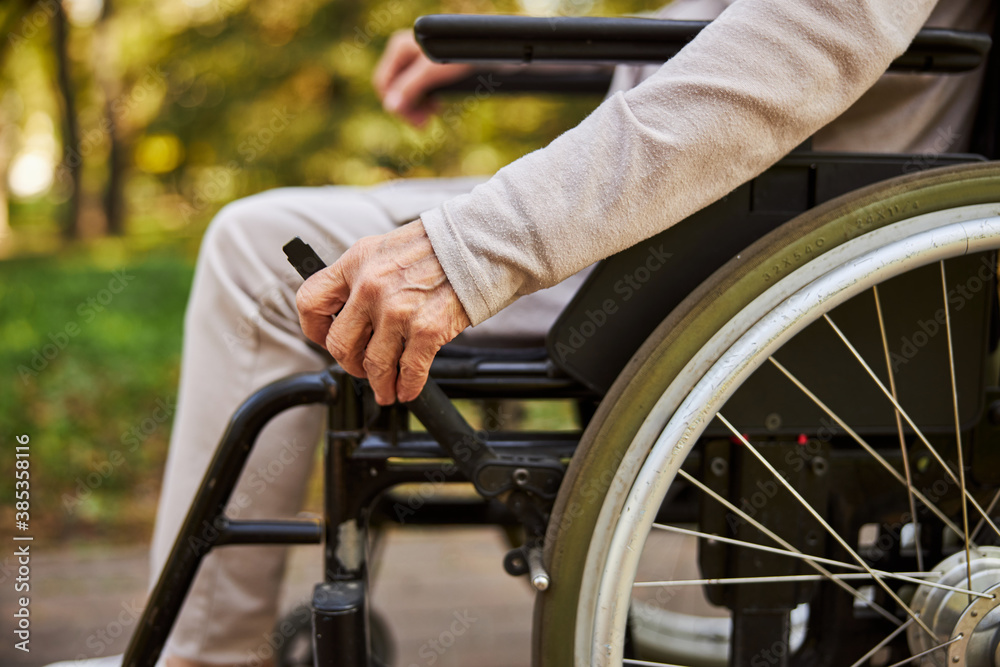Wrinkled hand on a wheelchair handle outdoors Wrinkled hand on a wheelchair handle outdoors